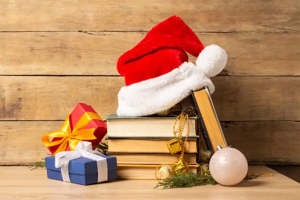 Pile of books, Santa Claus hat, Christmas-tree decorations and Gifts on a wooden background. Holiday concept, christmas, christmas eve.