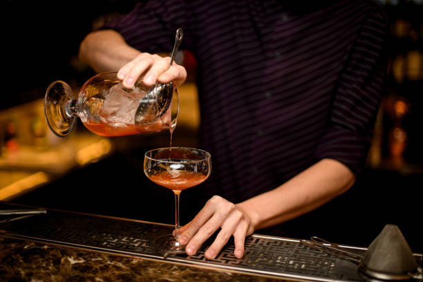 istock Professional bartender pouring a alcoholic drink from the the one glass with ice cube to another empty 1186567163