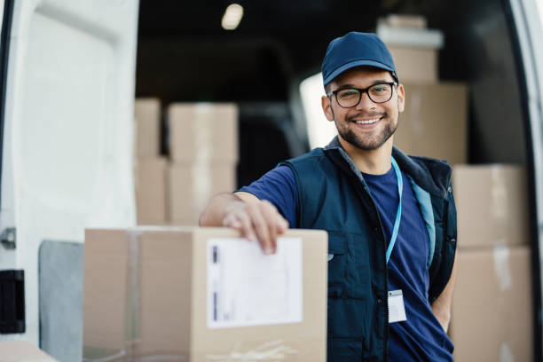 joven repartidor feliz con cajas de cartón mirando a la cámara. - bulto fotografías e imágenes de stock