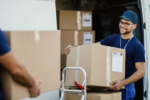 Happy manual worker unloading cardboard boxes from delivery van.