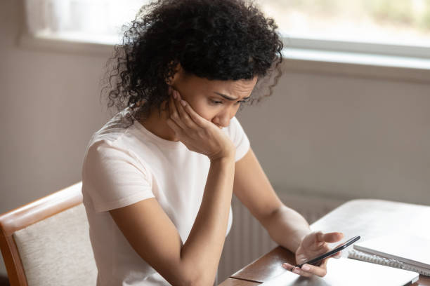 Frustrated biracial woman having operational cellphone problems Upset desperate african American millennial woman sit at table have software problems with cellphone, frustrated biracial female confused with smartphone breakdown, gadget malfunction or virus attack irritation photos stock pictures, royalty-free photos & images