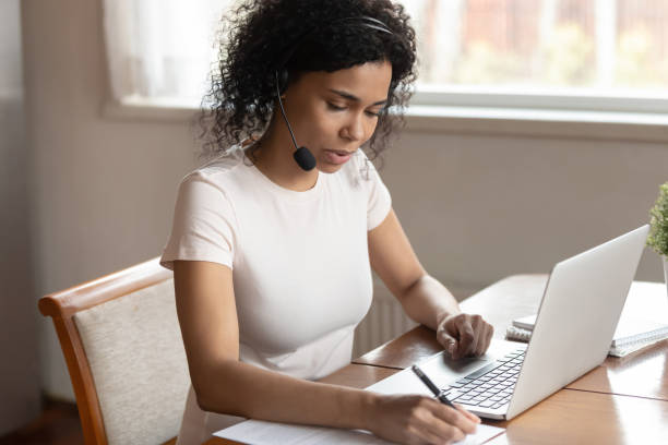 istock Serious female worker in headset making notes working on laptop 1186579776