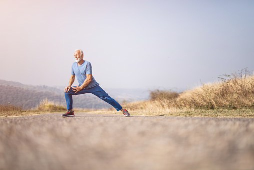 Athletic senior man exercising and stretching outdoors in nature
