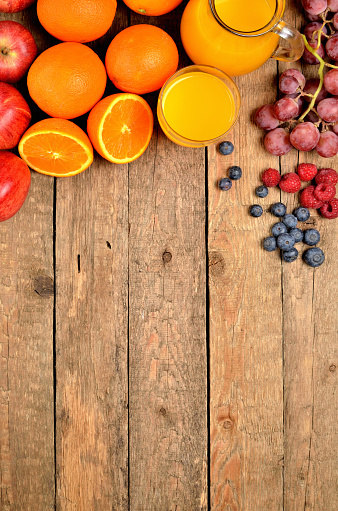 Orange juice, fresh oranges, apples, grapes, raspberries and blueberries on a wooden table - view from above - vertical photo