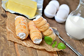 Custard tube of pastry filled with cream traditional czech sweet, butter, eggs, mint leaves and milk on wooden table