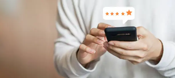 Photo of close up on customer man hand pressing on smartphone screen with gold five star rating feedback icon and press level excellent rank for giving best score point to review the service , technology business concept