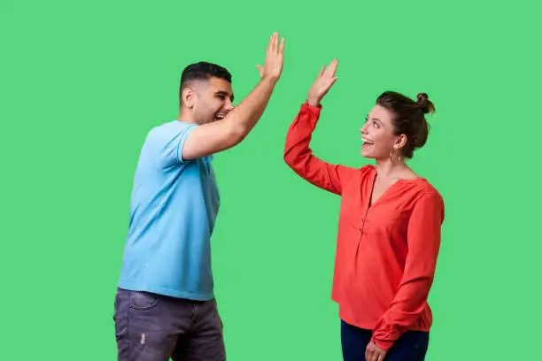 Photo of Side view portrait of excited amazed young couple in casual wear giving high five. isolated on green background