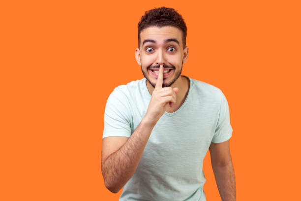 istock Please, keep silence! Portrait of positive brunette man asking to be quiet. indoor studio shot isolated on orange background 1186604591