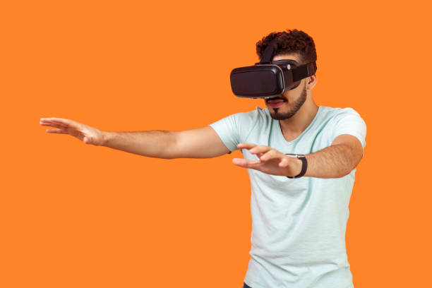 istock Portrait of attentive gamer, brunette man stretching arms forward while playing virtual reality game. isolated on orange background 1186604601