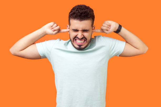 Don't want to listen anymore. Portrait of brunette man tightly covering his ears. isolated on orange background Don't want to listen anymore. Portrait of brunette man standing with irritated grimace, tightly covering his ears not to hear annoying loud sound. indoor studio shot isolated on orange background man closing ears photos stock pictures, royalty-free photos & images