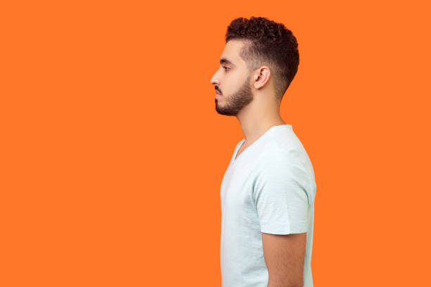 istock Side view of serious handsome brunette man looking left, empty copy space for text. indoor studio shot isolated on orange background 1186604622