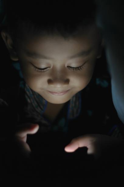 istock Asian smiling boy is playing smartphone in the dark blanket 1186609782