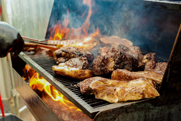a barbecue with pieces of meat on fire with smoke a barbecue with pieces of meat on fire and a hand taking a piece brazilian bbq stock pictures, royalty-free photos & images