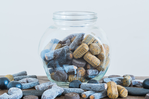Candy jar in centre of table filled with assorted double salted licorice, salmiak, salmiakki, with white background