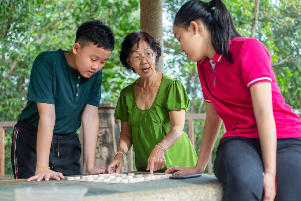 abuela enseñando a los nietos jugando ajedrez chino o xiangqi en un jardín - chinese chess fotografías e imágenes de stock