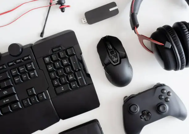 Photo of gamer work space concept, top view a gaming gear, mouse, keyboard, joystick, headset, mobile joystick, in ear headphone and mouse pad on black table background.