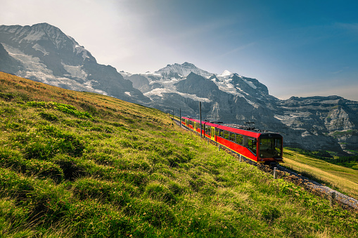 Spectacular cogwheel railway with popular electric red tourist train. High snowy Jungfrau mountain with glaciers and red passenger train, Kleine Scheidegg, Grindelwald, Bernese Oberland, Switzerland, Europe