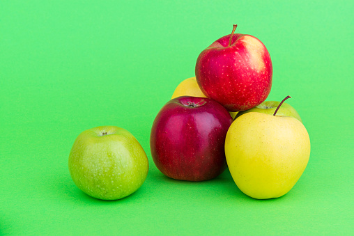 Heap of different kinds of apples on green background