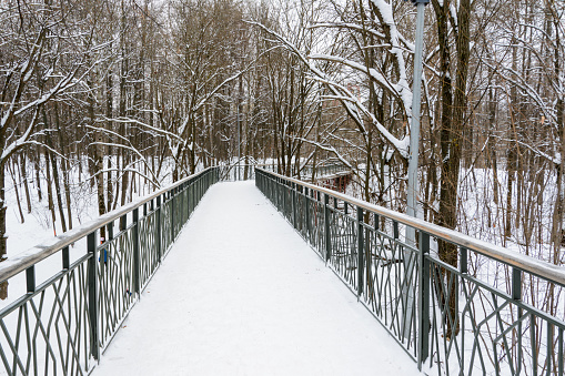 Snow-covered, pedestrian bridge over a ravine in the winter forest. Lots of snow on a beautiful road towards the forest.