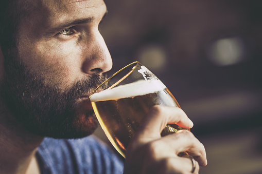 Close up of mid adult man drinking beer in a bar and looking away.