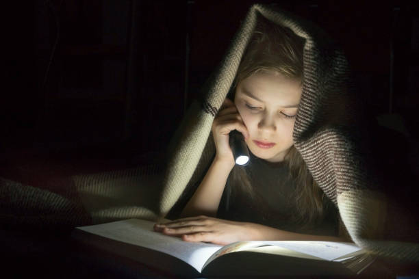 istock Girl with a flashlight reading a book under a blanket at night. 1186671005