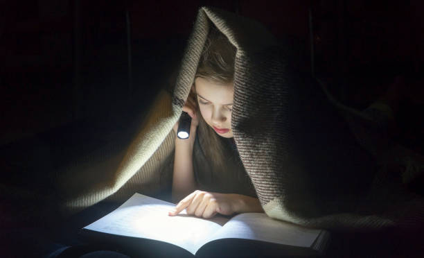 istock Girl with a flashlight reading a book under a blanket at night. 1186671006