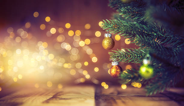 Christmas tree decorated with golden & green ornaments on wood floor. Defocused lights in the background.