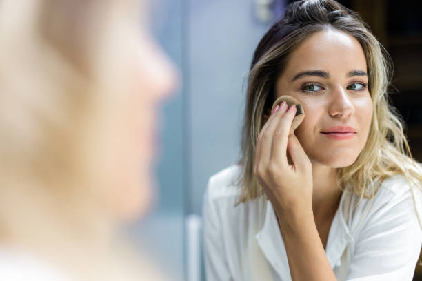 réflexion dans un miroir d'une femme appliquant la poudre de visage dans la salle de bains. - make up foundation cosmetics face powder photos et images de collection