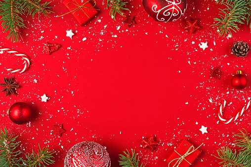Christmas or Happy New Year red background. Frame made of fir tree branches, holiday decorations and gift boxes with snow on red background. flat lay. top view with copy space
