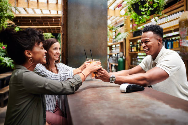 Great bartenders make everyone feel like VIP Shot of a young man serving two young women drinks at a bar pub bar counter bar men stock pictures, royalty-free photos & images