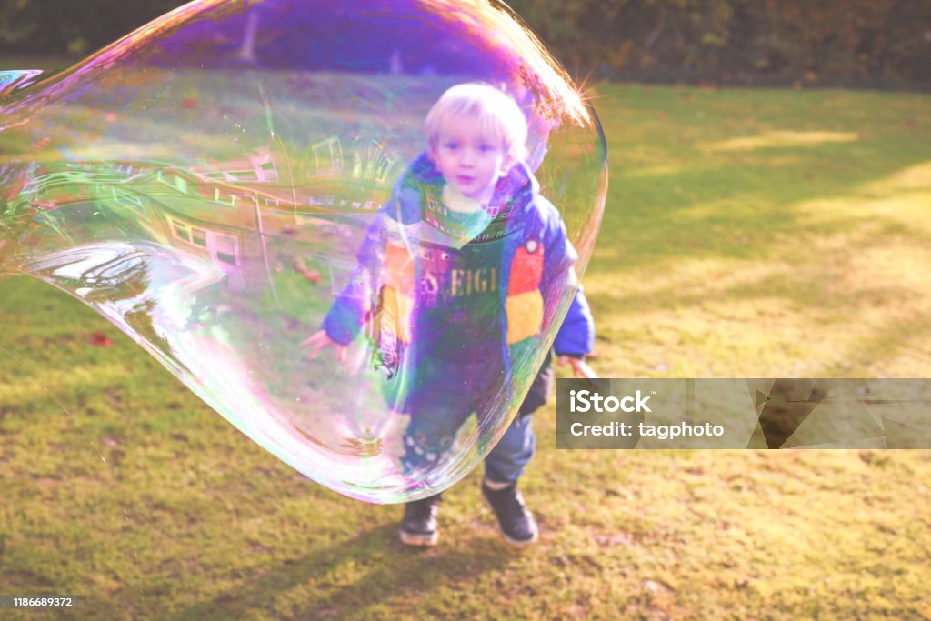 Child playing outside in a garden during day time with bubbles he is happy and running Activity Stock Photo