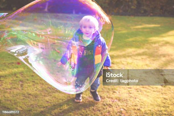 Child Playing Outside In A Garden During Day Time With Bubbles He Is Happy And Running Stock Photo - Download Image Now