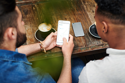 Shot of two young men chatting and using their smartphones in a cafe