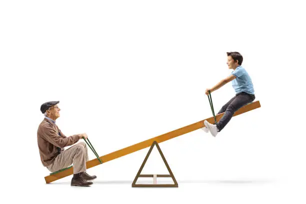 Full length profile shot of a child playing on a seesaw with his grandfather isolated on white background