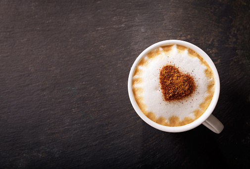 Valentines day.  Cup of cappuccino coffee with drawn heart on dark background, top view