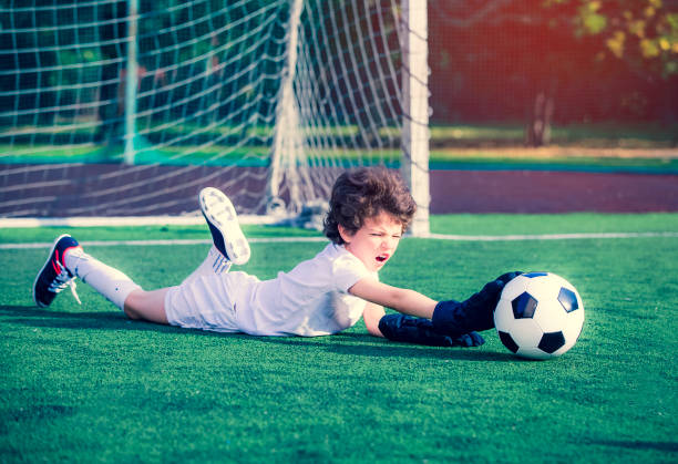 junge fußball-goalie versucht, eine rettung zu machen. kleiner fußballtorwart mit handschuhen. kinder - fußball-champion. junge torwart in fußball-sportbekleidung auf stadion mit ball. sportkonzept. - playing field goalie soccer player little boys stock-fotos und bilder