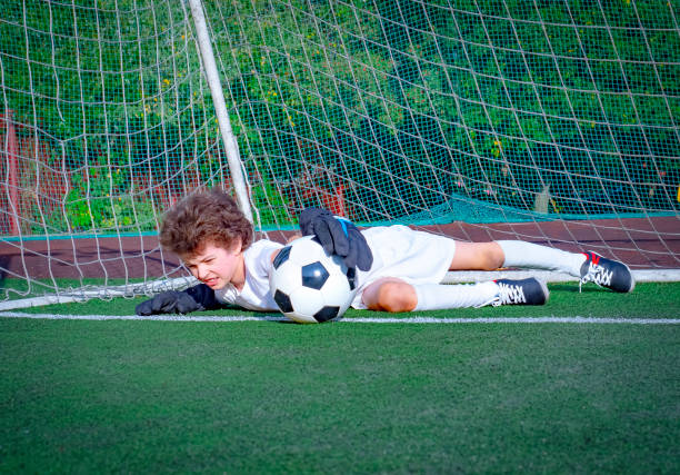 junge fußball-goalie versucht, eine rettung zu machen. kleiner fußballtorwart mit handschuhen. kinder - fußball-champion. junge torwart in fußball-sportbekleidung auf stadion mit ball. sportkonzept. - playing field goalie soccer player little boys stock-fotos und bilder