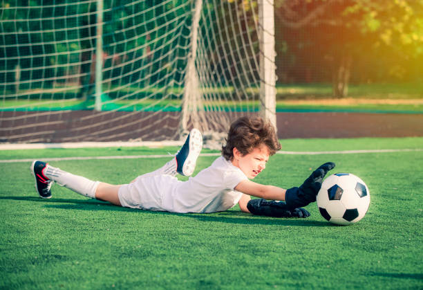 junge fußball-goalie versucht, eine rettung zu machen. kleiner fußballtorwart mit handschuhen. kinder - fußball-champion. junge torwart in fußball-sportbekleidung auf stadion mit ball. sportkonzept. - playing field goalie soccer player little boys stock-fotos und bilder