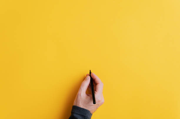 istock Male hand writing on a blank yellow surface with black marker 1186700760