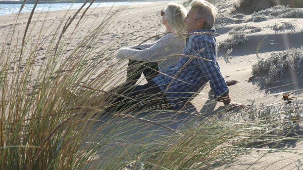dojrzała para relaksuje się na plaży o wschodzie słońca - sunrise beach couple hiking zdjęcia i obrazy z banku zdjęć
