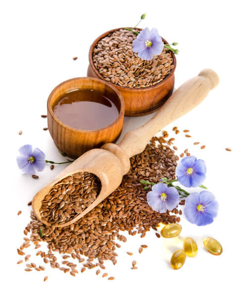 Flax seeds in the wooden scoop, bowl with oil and oil in caps and  beauty flowers isolated on white background. Phytotherapy stock photo