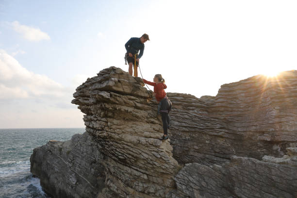 les amis montent la caractéristique côtière de roche au lever de soleil - mountain climbing rock climbing motivation awe photos et images de collection