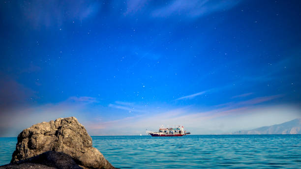 FERRY BOAT TRANSPORT PASSENGERS DURING SEA JOURNEY IN EVENING TIME , WONDERFUL GOLDEN SKY LIGHT BEFORE SUNSET , TWILIGHT CLOUD BACKGROUND