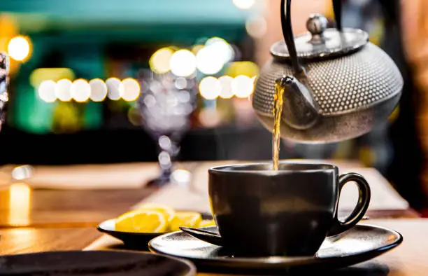 Photo of metal teapot pour black tea in black glass mug in cafe