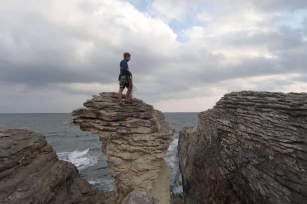 istock Young man throws rock from coastal rock feature at sunrise 1186727406