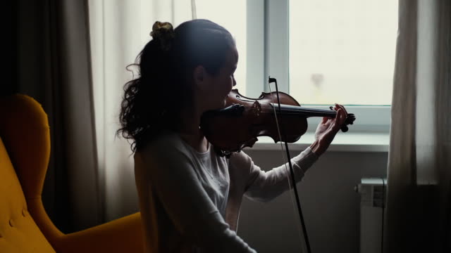 Beautiful young woman musician playing the violin by the window