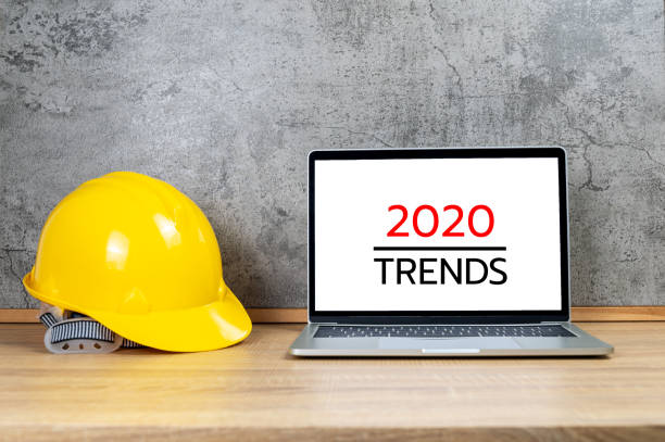 Yellow safety helmet and laptop computer with 2020 TRENDS text on white screen stock photo