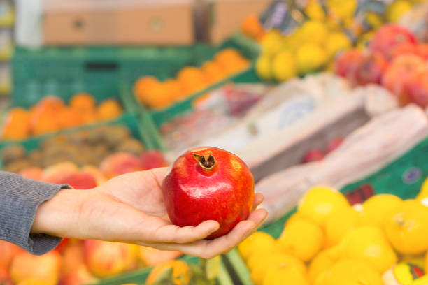 istock Woman's hand choosing pomegranate at supermarket 1186732517