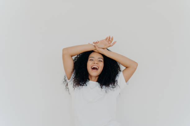 istock Overjoyed curly haired young lady keeps both hands on forehead, opens mouth and laughs happily, feels energetic, dressed in casual wear, poses against white studio background. What funny joke! 1186734328