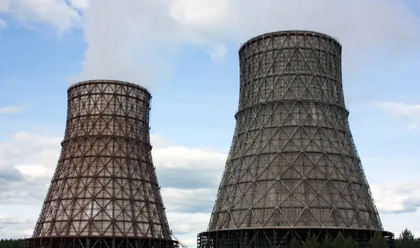 Photo of Thermal power station, cogeneration plant, two cooling towers from which smoke comes. Blue sky with clouds